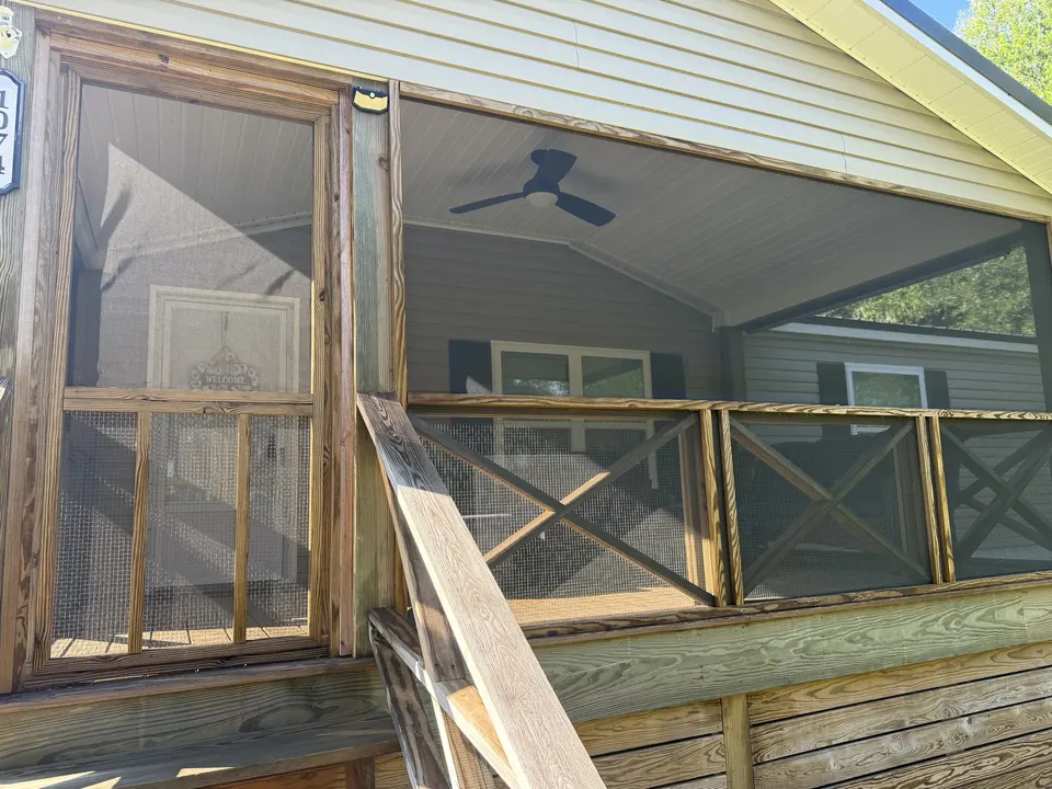 Covered front porch entry at Sapelo House with a screened door, railing, and ceiling fan.