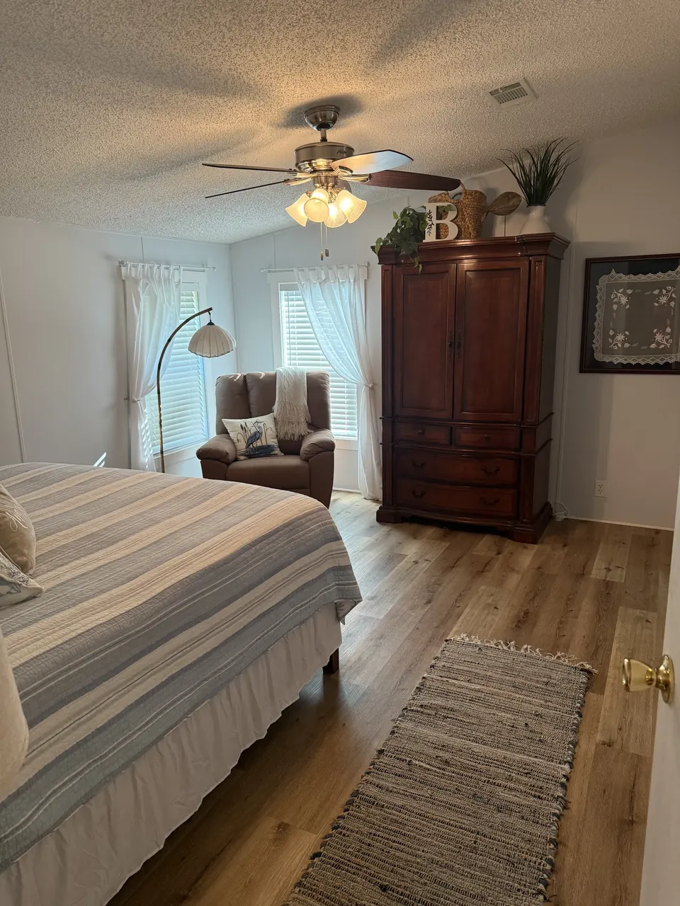 Primary bedroom at Sapelo House with a striped bed, wood floors, and a cozy sitting area by the window.