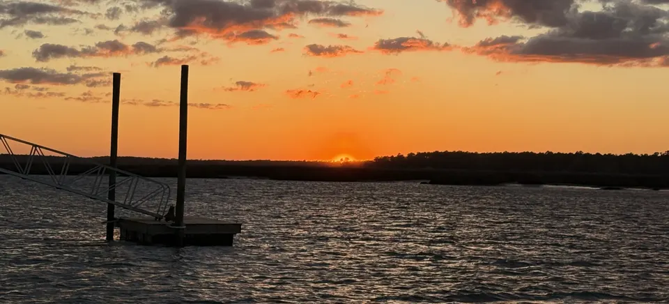 Orange sunset over the Sapelo River with dramatic clouds and a dock in the foreground in coastal Georgia.